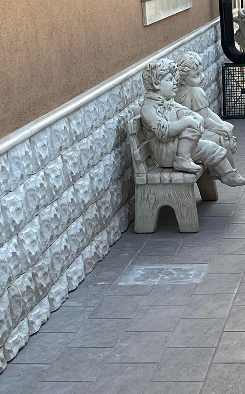 Un paio di statue di bambini seduti su una panchina.