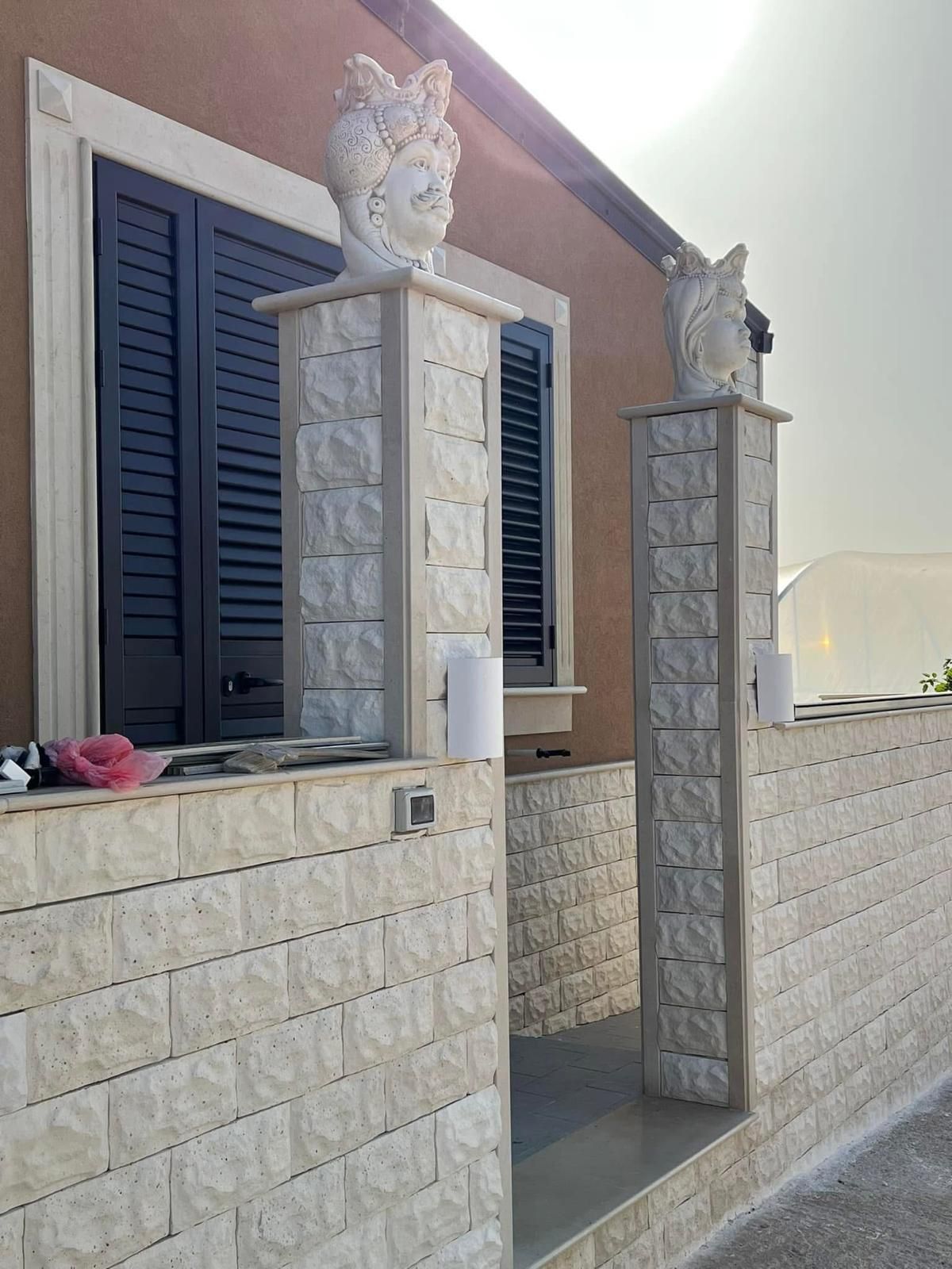 Un muro di mattoni con colonne e una finestra con persiane nere