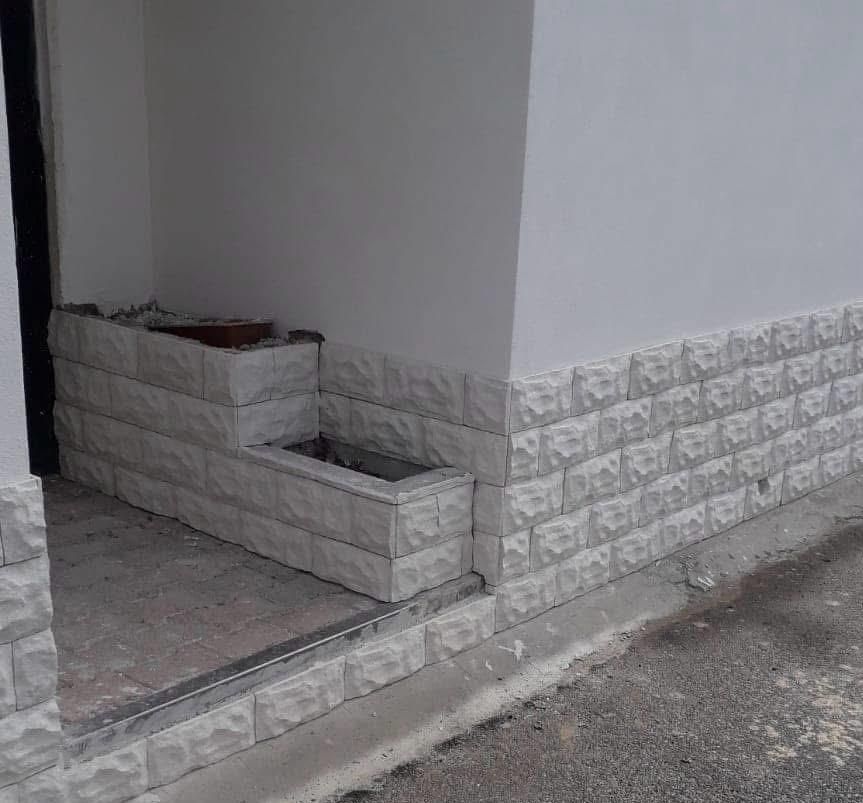 Un muro di mattoni bianchi con una fioriera in un angolo.