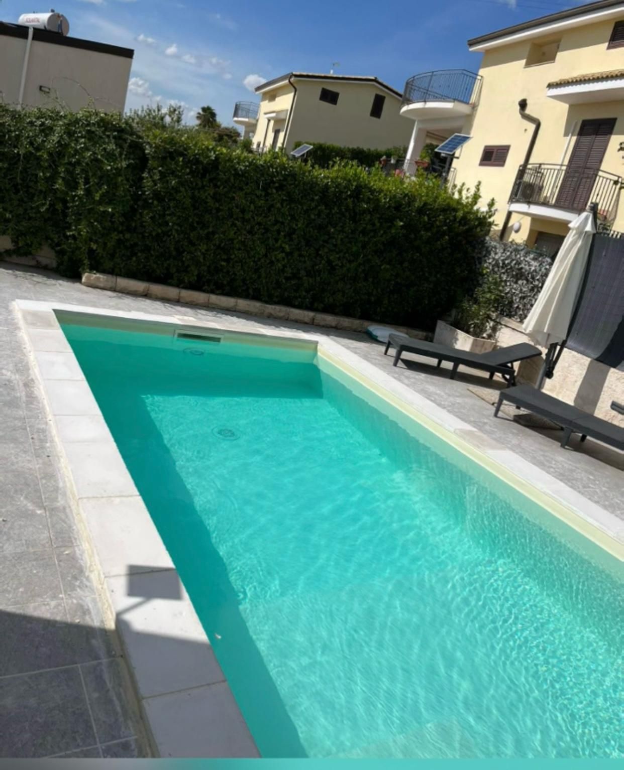 Una grande piscina circondata da sedie e una siepe