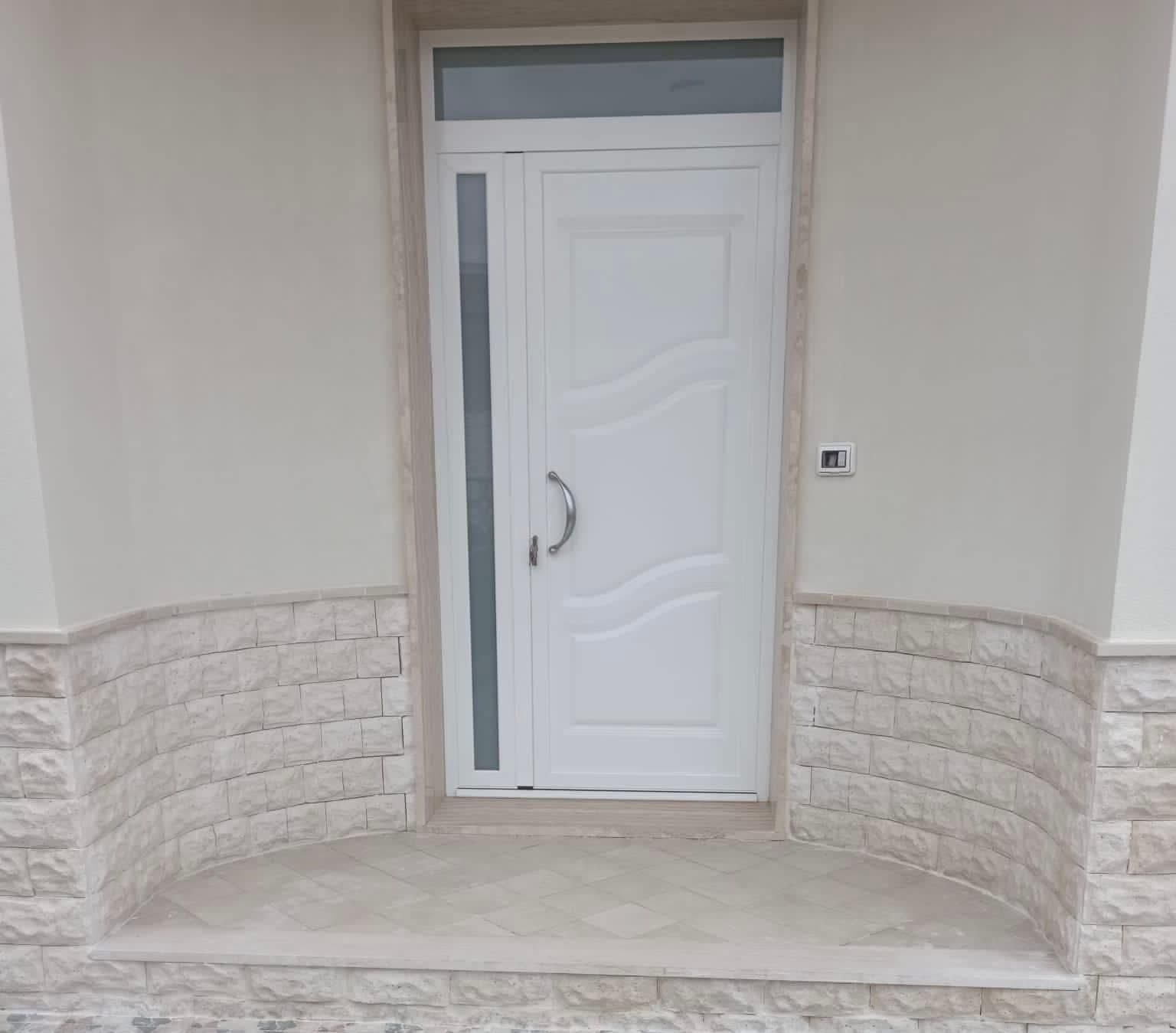 Una porta bianca con una finestra di vetro si trova su un muro di mattoni.