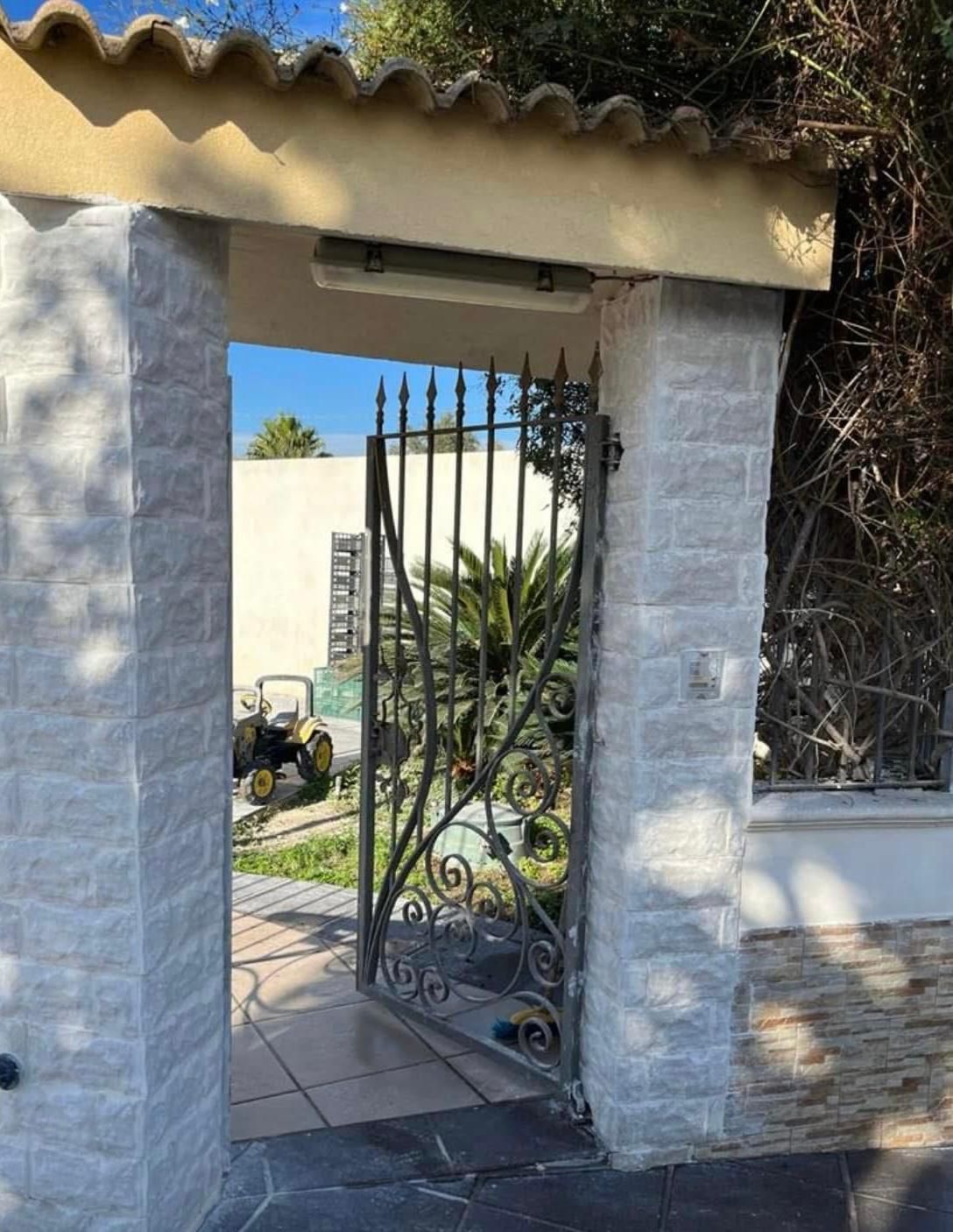 Un muro di mattoni bianchi con un cancello in ferro battuto che conduce a una casa.