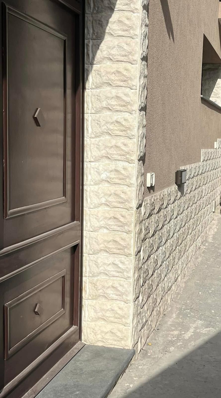 Una porta marrone è appoggiata sul lato di un edificio, accanto a un muro di mattoni.