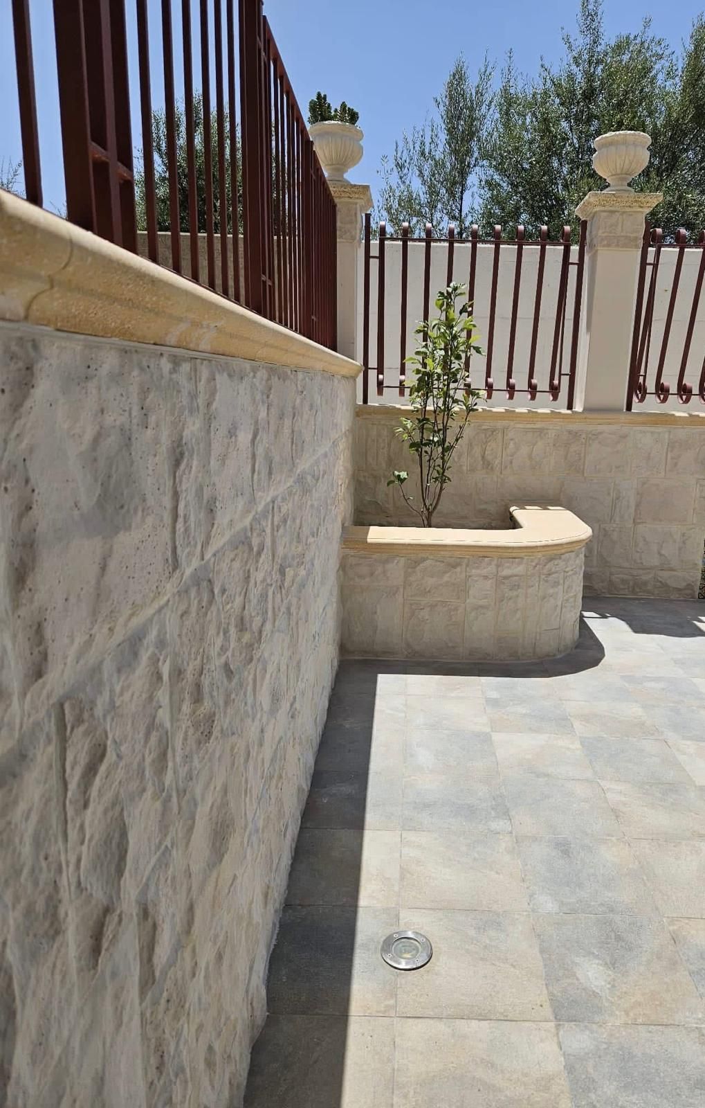 Un muro di pietra con una recinzione sullo sfondo e una panchina in primo piano.