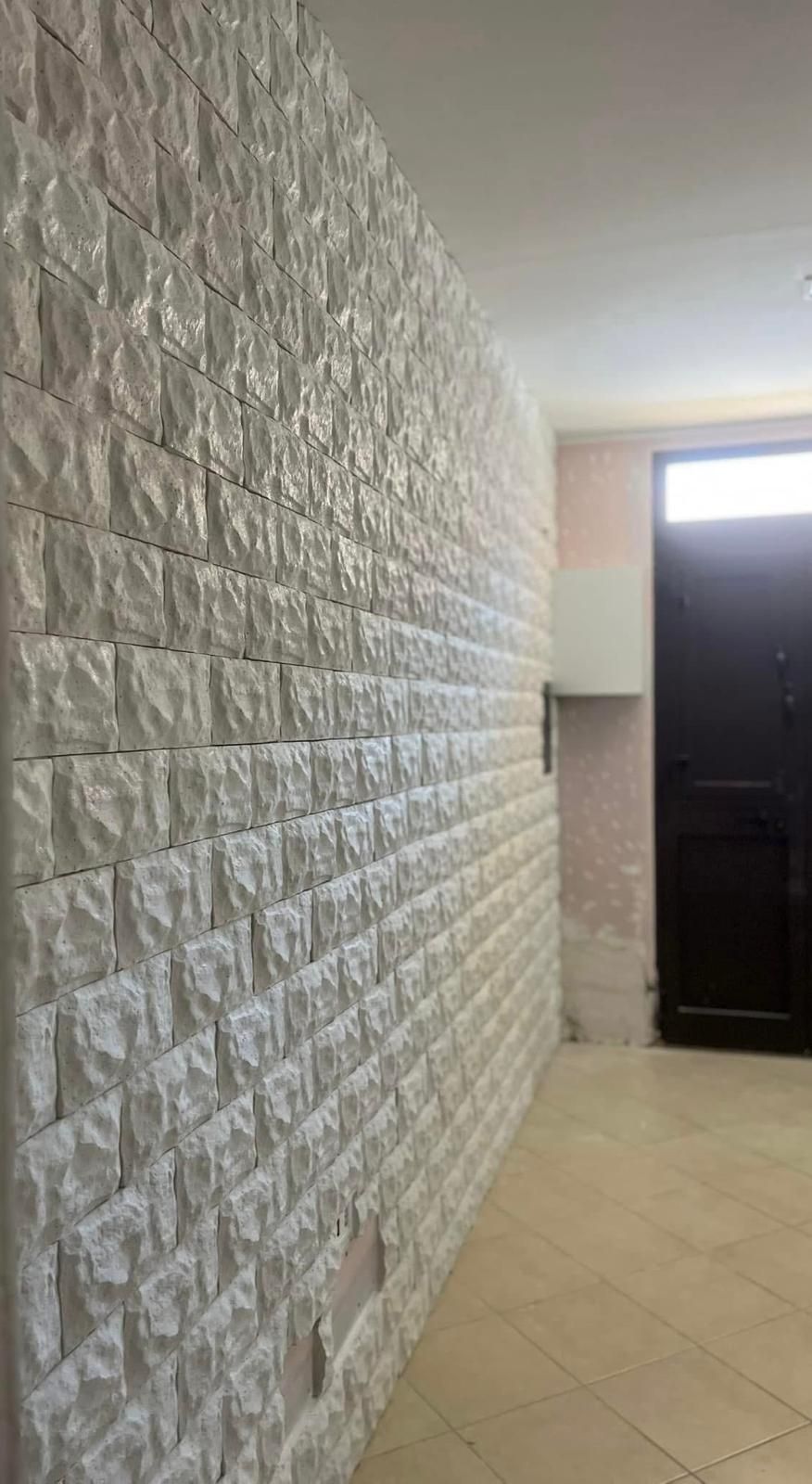Un lungo corridoio con un muro di mattoni bianchi e una porta nera.