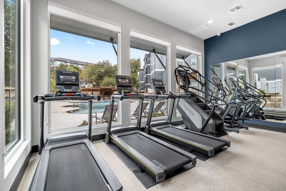 a gym with treadmills, stairs, and a large mirror at Marquis at Crown Ridge in San Antonio, TX.