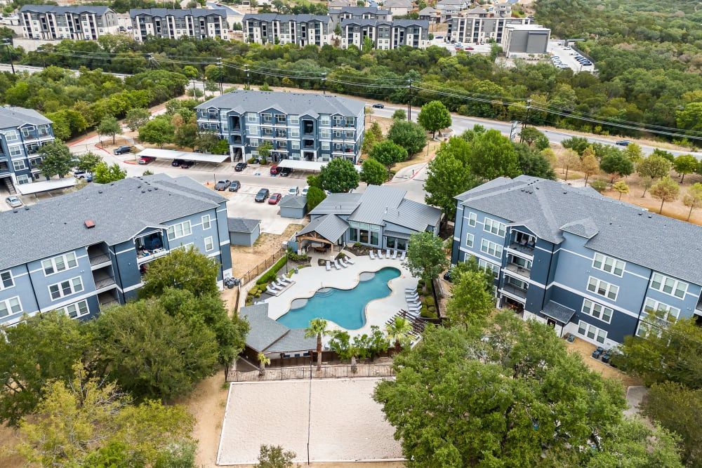 an aerial view of a large apartment complex with a swimming pool surrounded by trees at Marquis at Crown Ridge in San Antonio, TX.