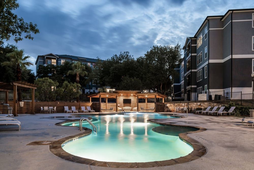 a large swimming pool is lit up at night in front of a building at Marquis at Crown Ridge in San Antonio, TX.