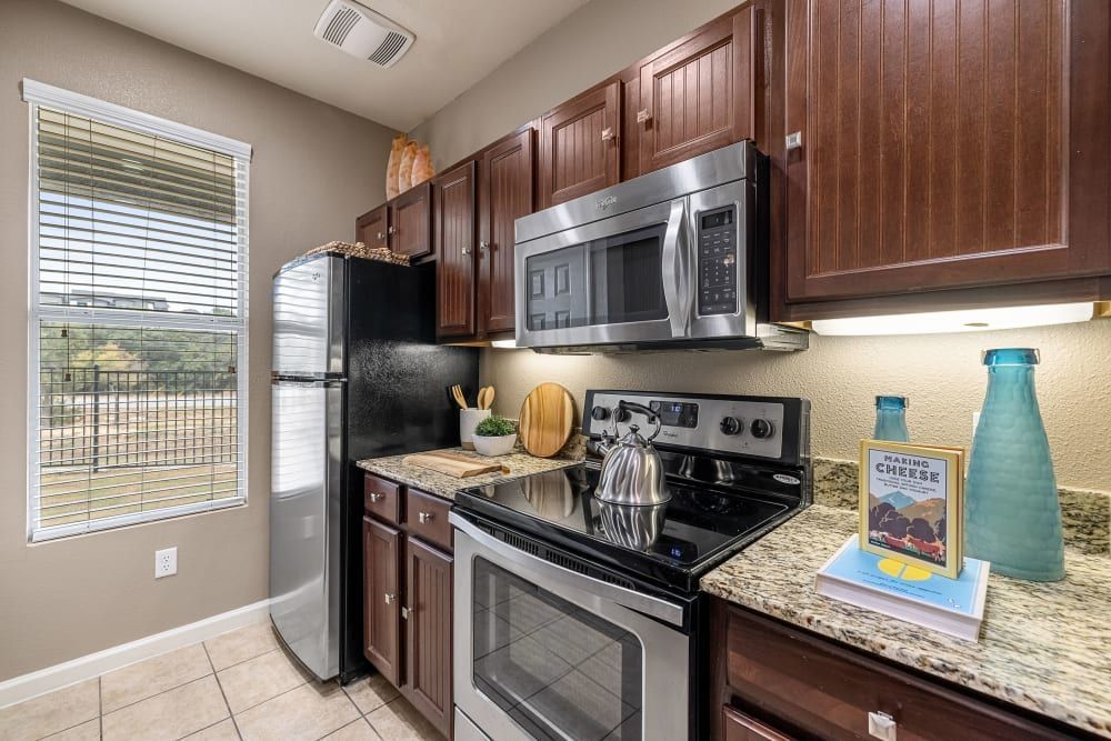 a kitchen with stainless steel appliances, granite counter tops, and wooden cabinets at Marquis at Crown Ridge in San Antonio, TX.