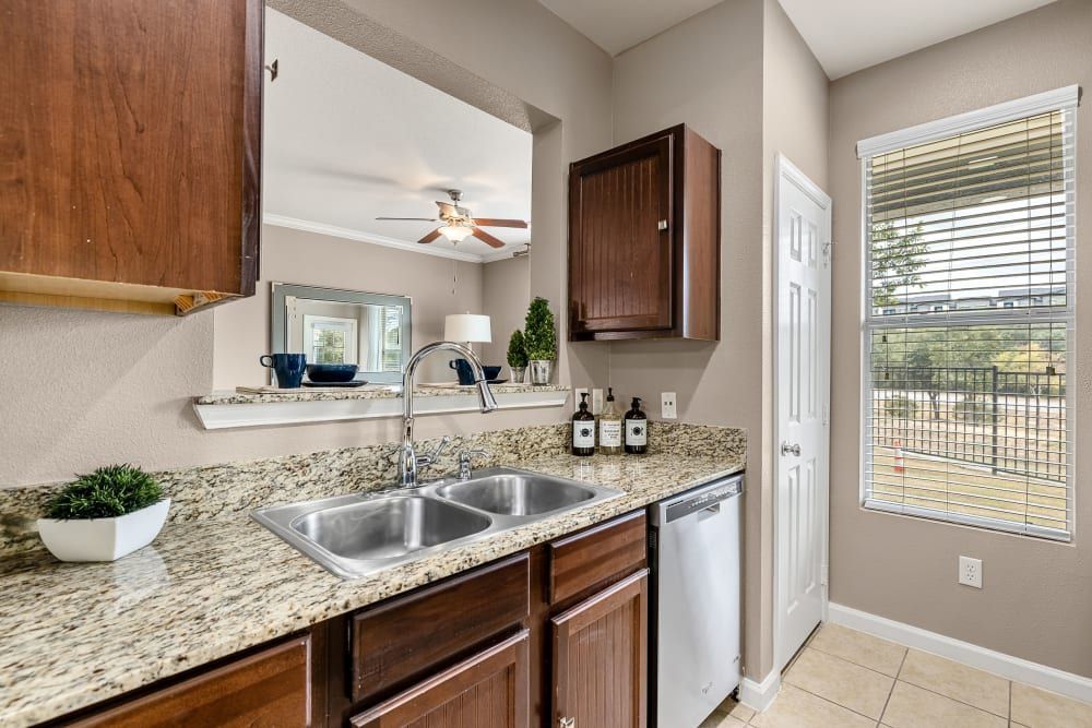 a kitchen with two sinks, a dishwasher, a ceiling fan, and a window at Marquis at Crown Ridge in San Antonio, TX.