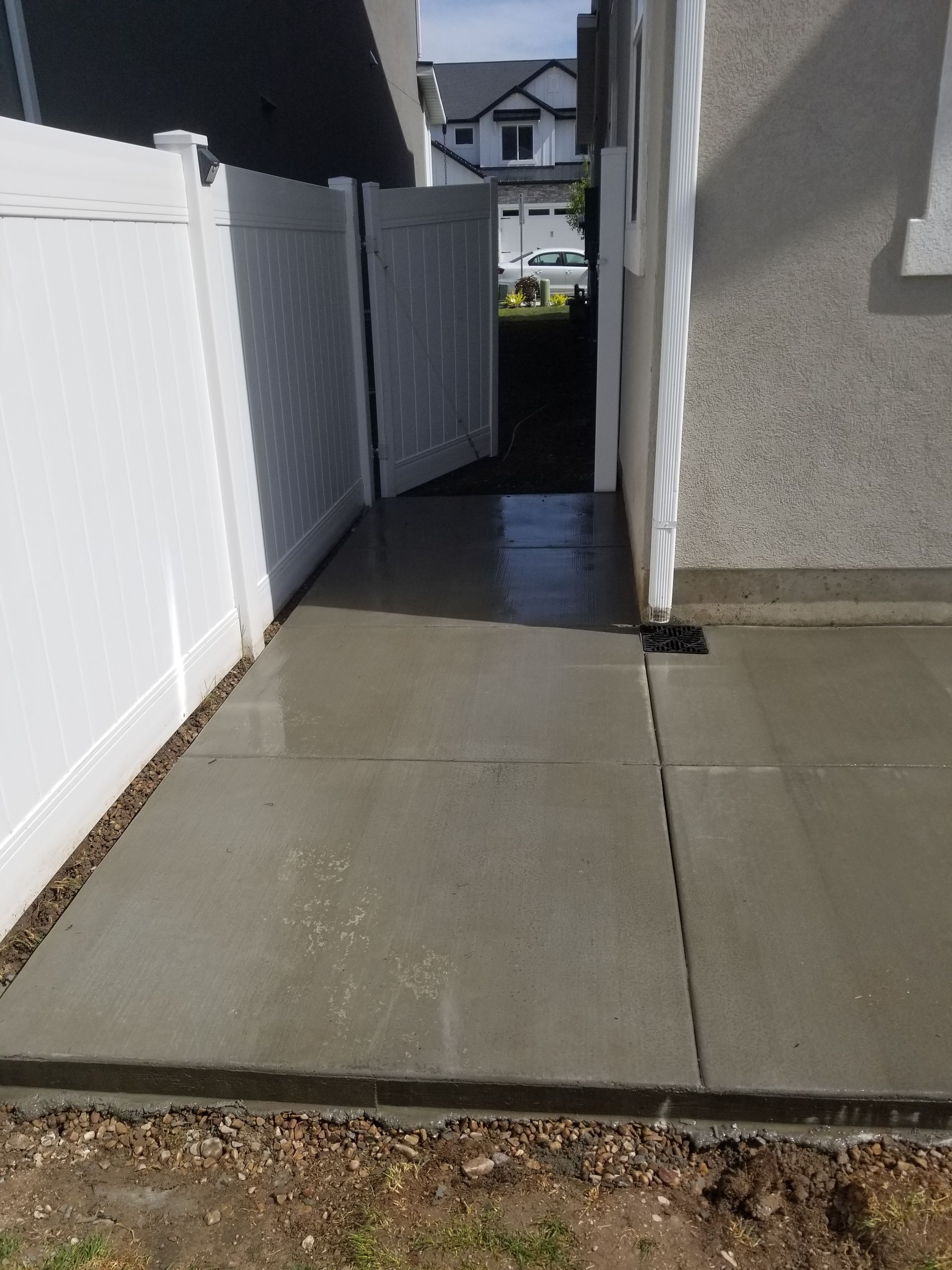 A concrete walkway leading to a house with a white fence.
