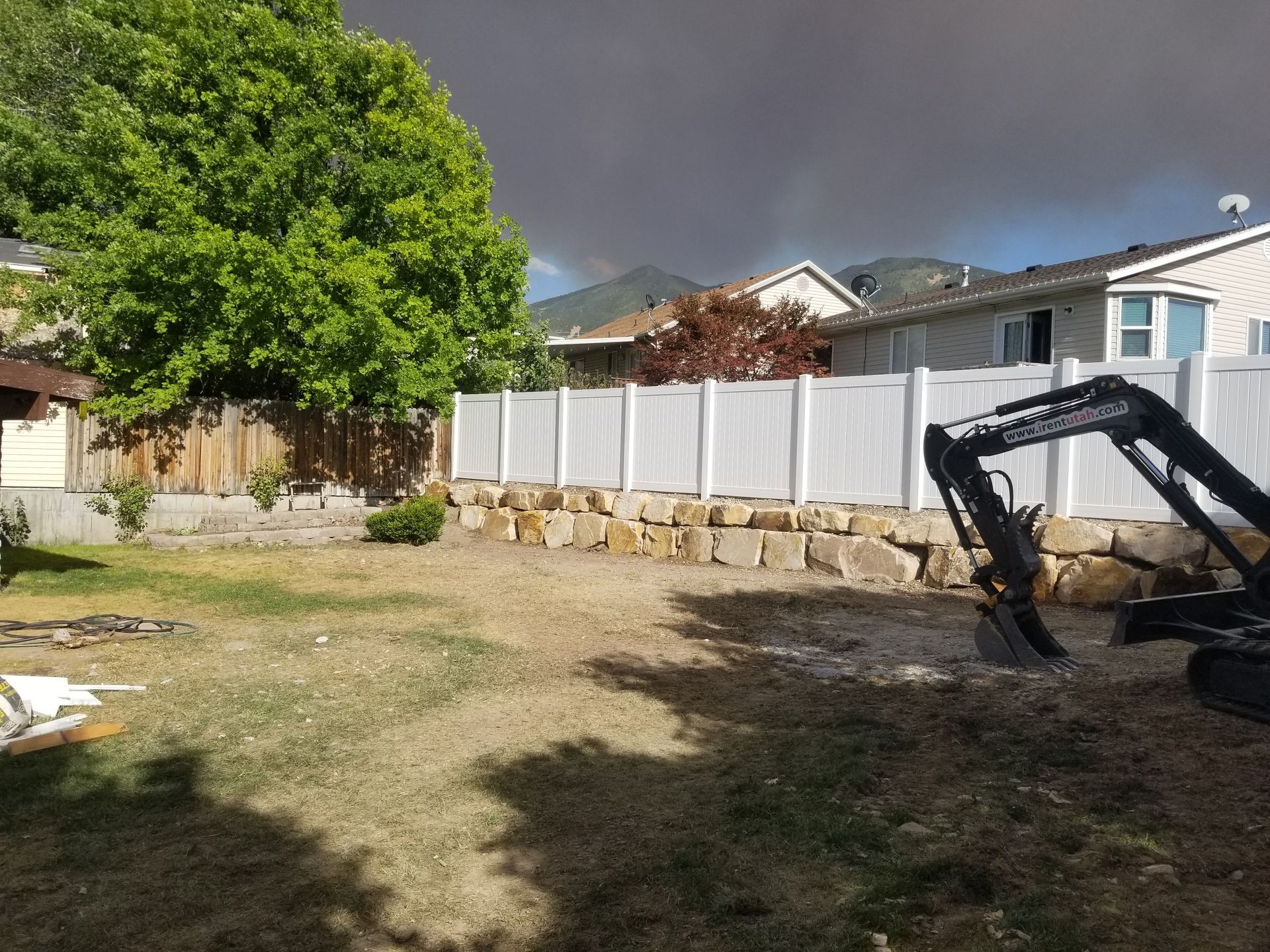 A backyard with a fence and a bulldozer in front of a house.