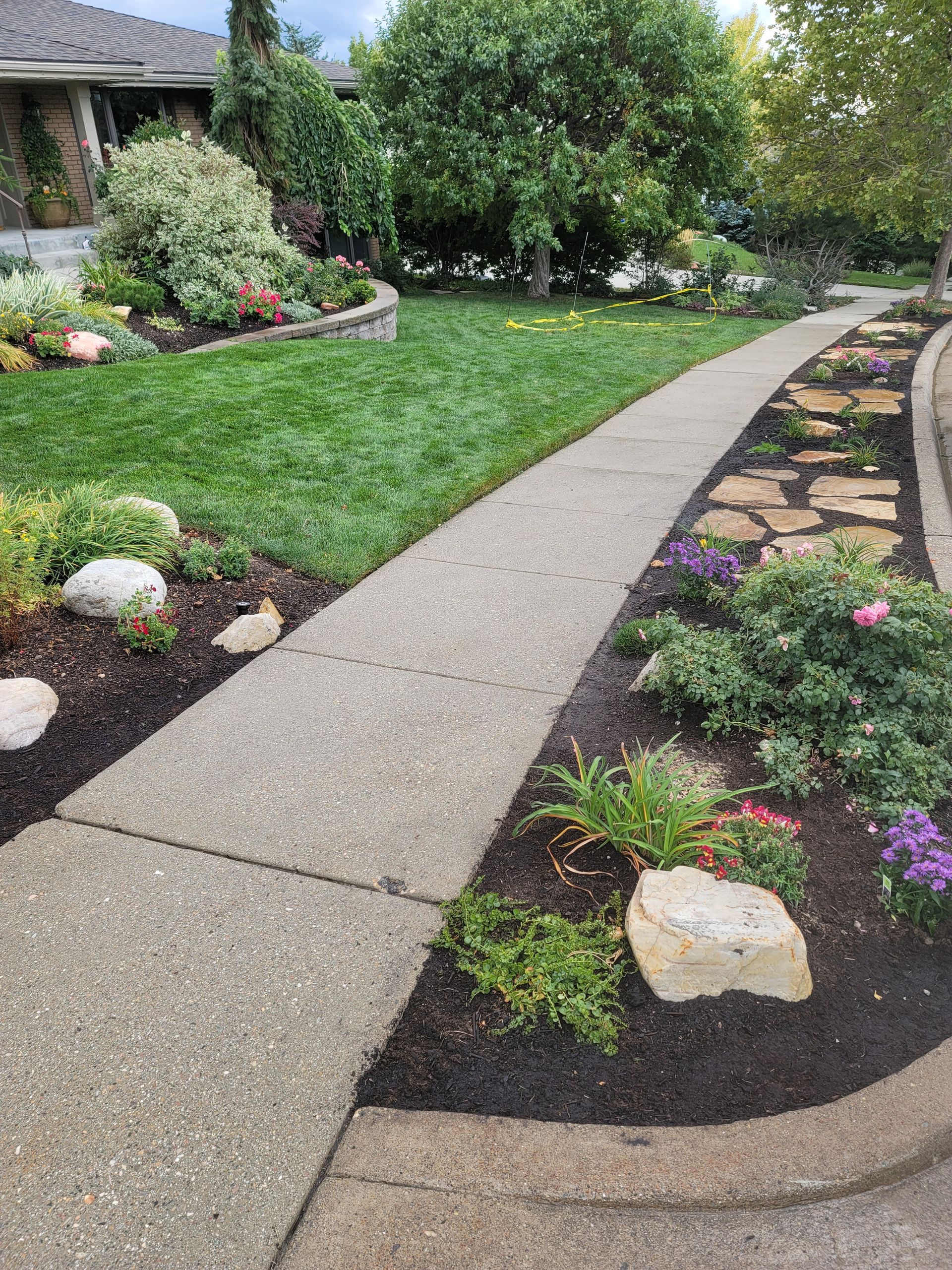 A sidewalk leading to a house surrounded by flowers and rocks.