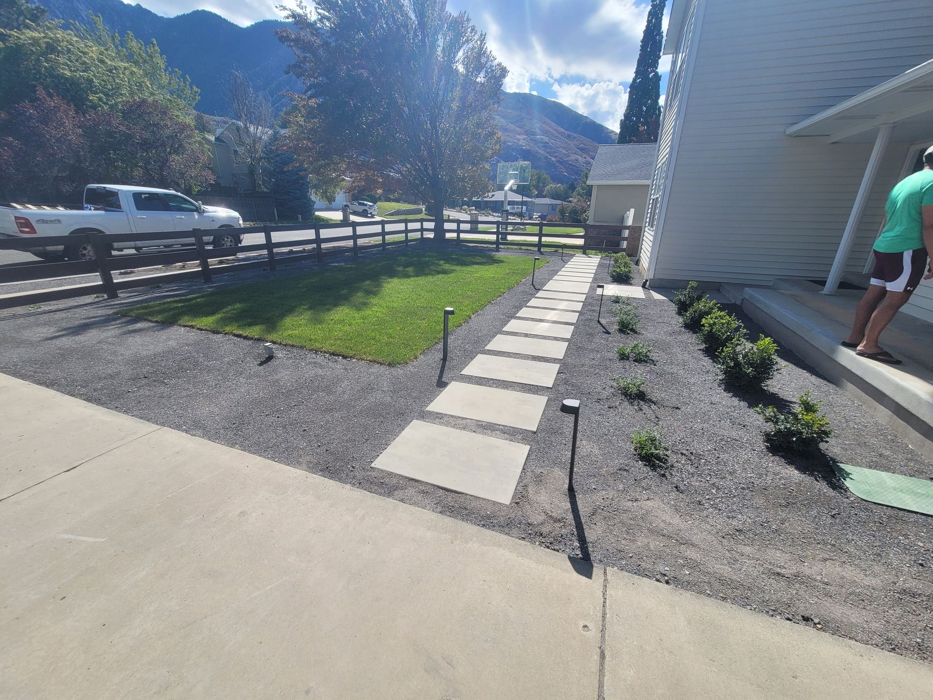 A fence surrounds a lush green yard with mountains in the background.