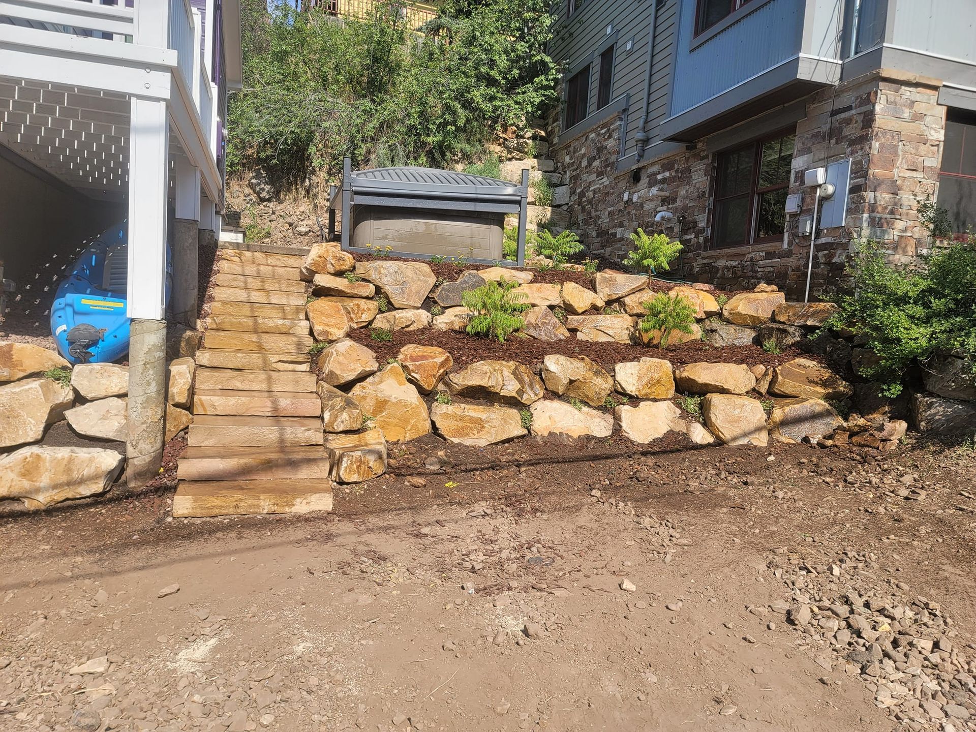 Stone retaining wall with steps leading up to a house with a garden bed and bench.