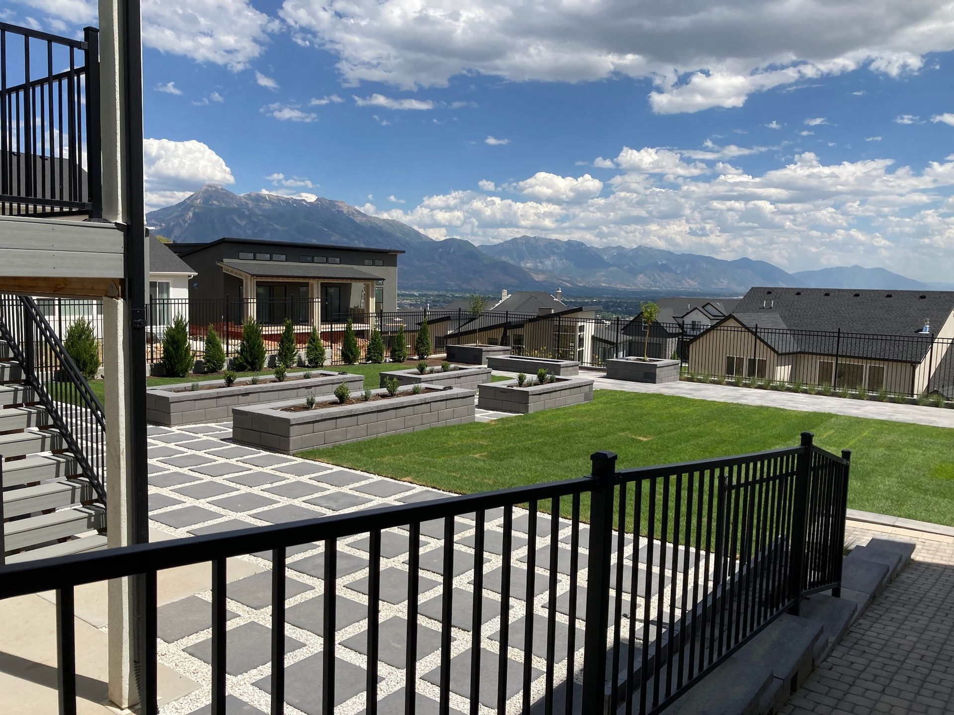 A fence surrounds a lush green yard with mountains in the background.