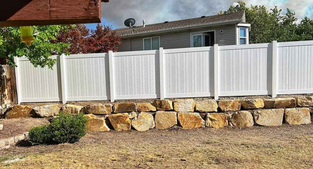 A white fence is sitting on top of a rock wall in front of a house.