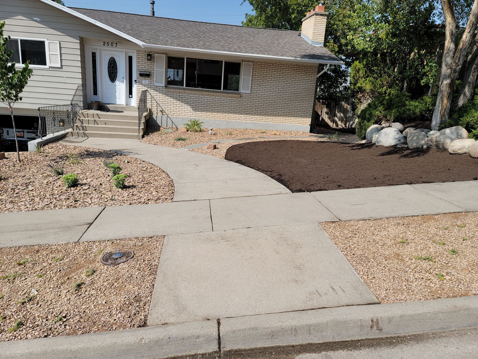 Sidewalk leading to a house with stone facade and new mulch landscaping.