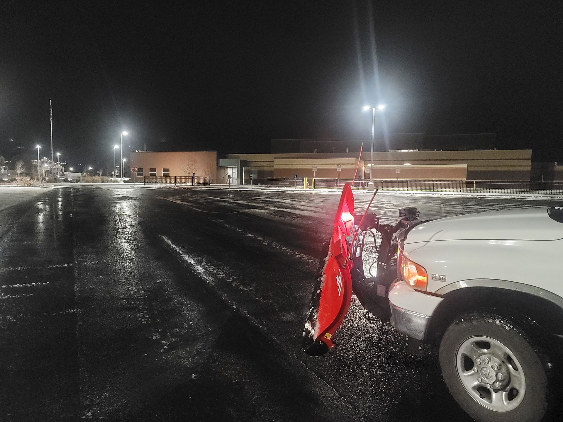 A snow plow is attached to the back of a truck in a parking lot at night.