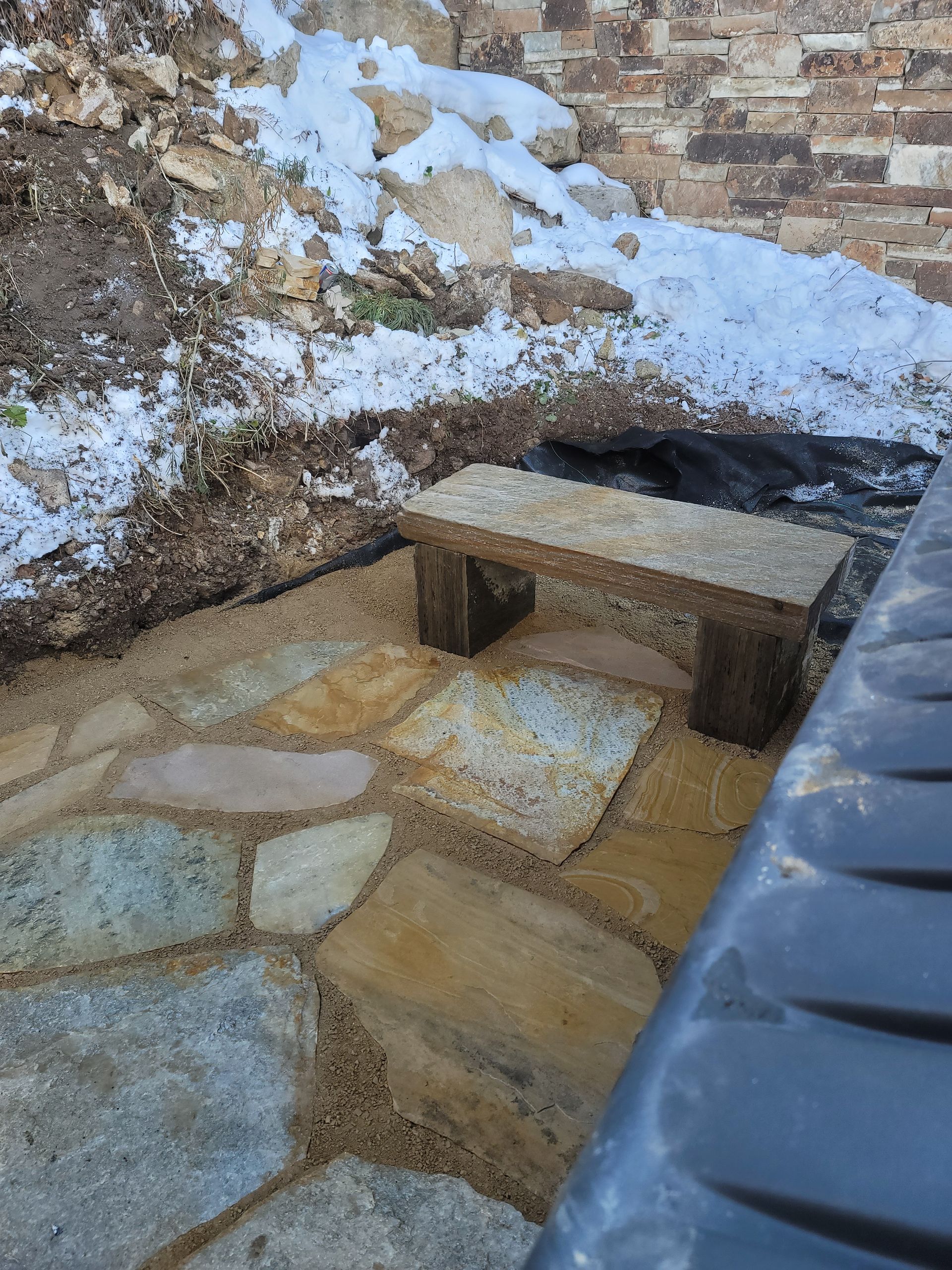 A stone bench is sitting on a stone patio next to a brick wall.