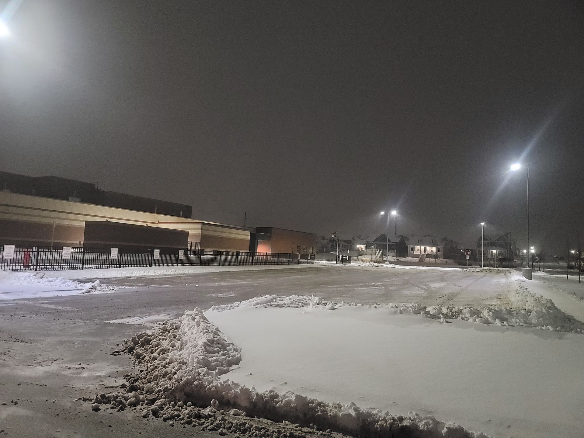 A snowy parking lot at night with a building in the background