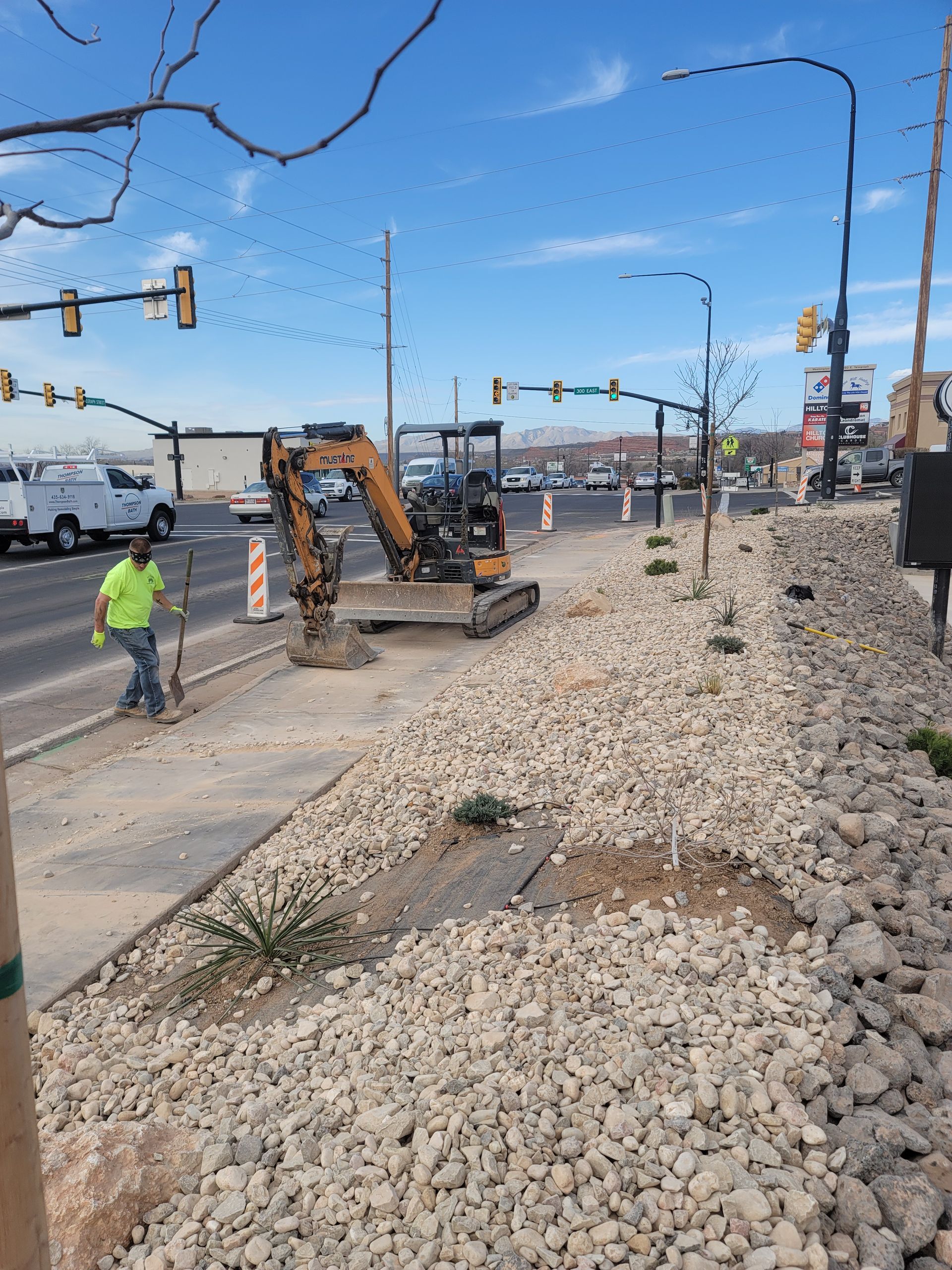 A man is walking across a gravel road next to a construction vehicle.