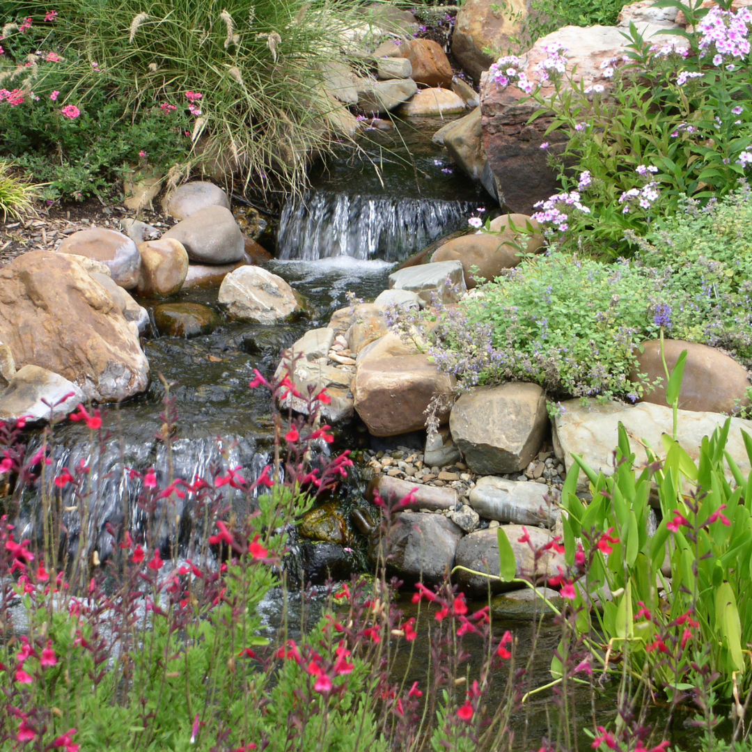 A waterfall surrounded by rocks and flowers in a garden