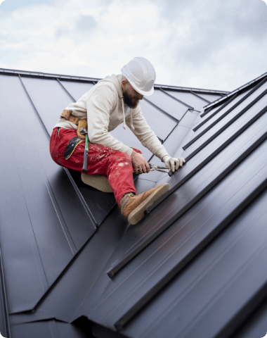 A man is kneeling on top of a metal roof.