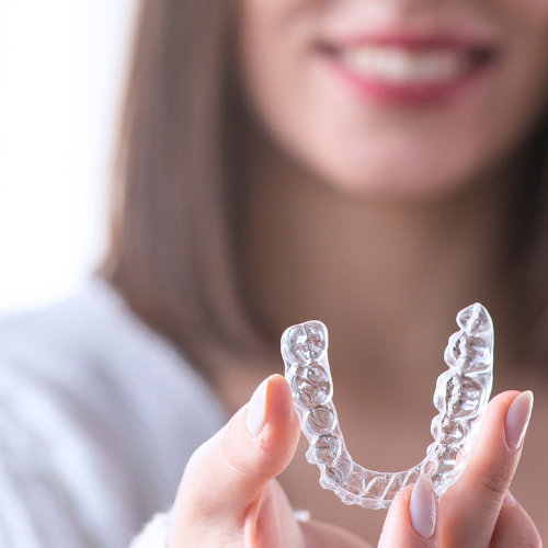 Woman smiling, holding a set of clear aligners. Woman showing clear aligners.