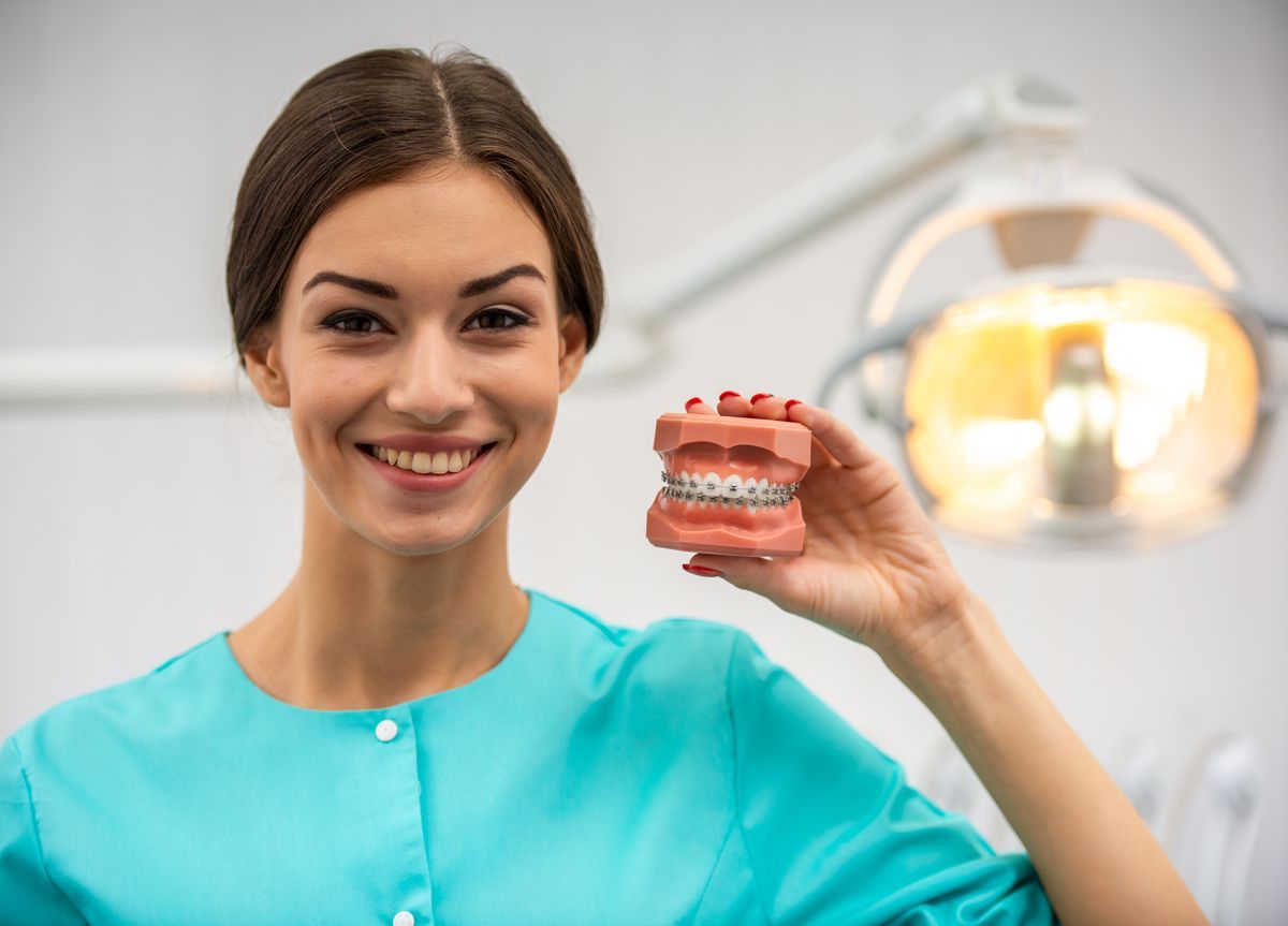 Smiling dentist holding a dental model in a clinic, with an exam light in the background