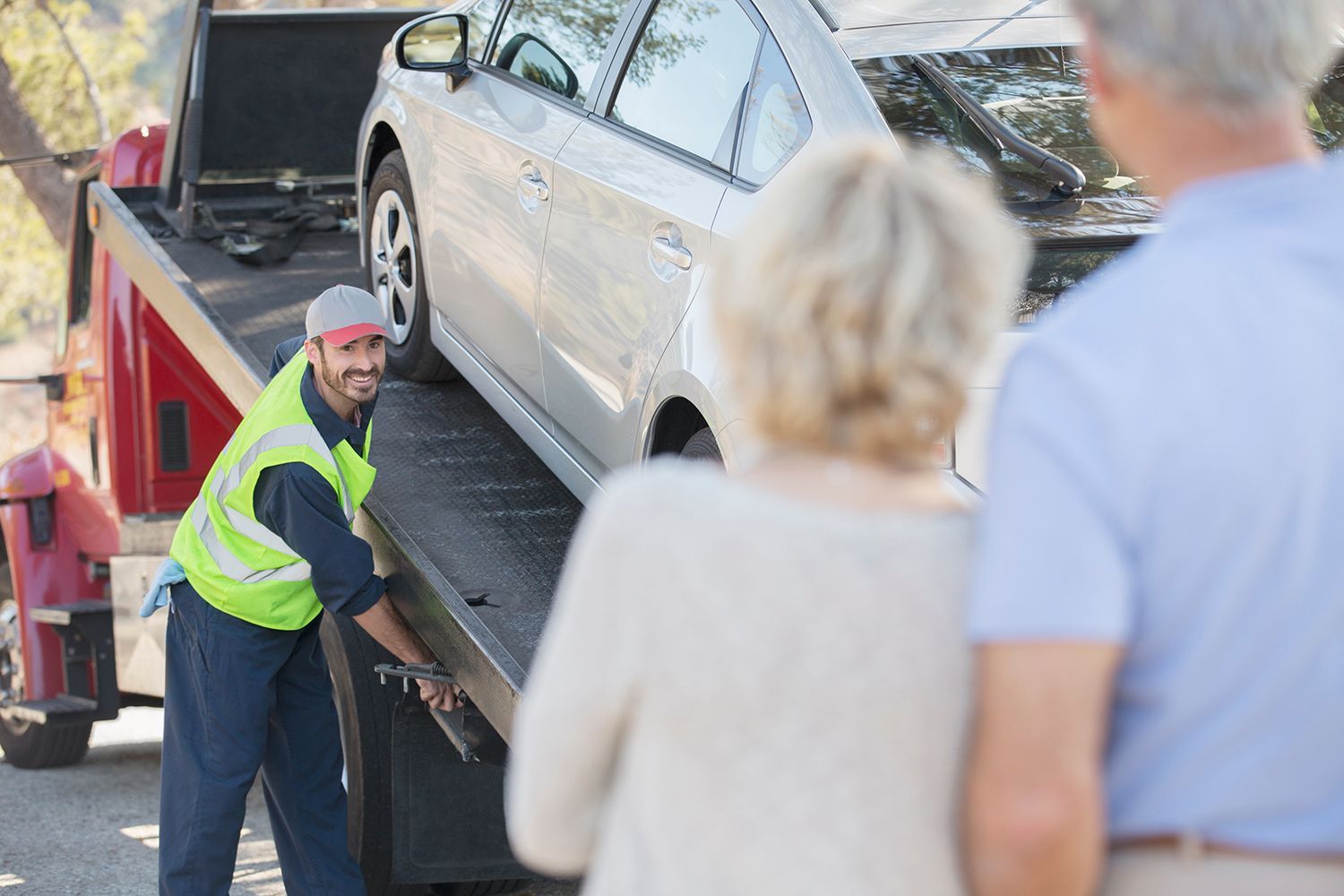 A tow truck operator secures a car on a flatbed, demonstrating a 24/7 towing service in action. A tow truck operator secures a car on a flatbed, demonstrating a 24/7 towing service in action.