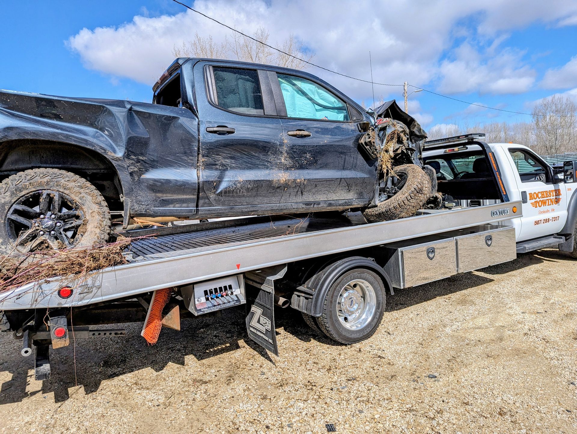 Tow truck towing a white car, the front wheel is secured in the tow apparatus on a paved surface.