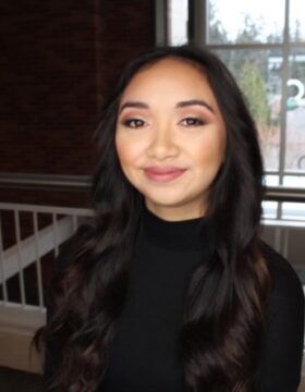 A woman in a black shirt is smiling in front of a window.