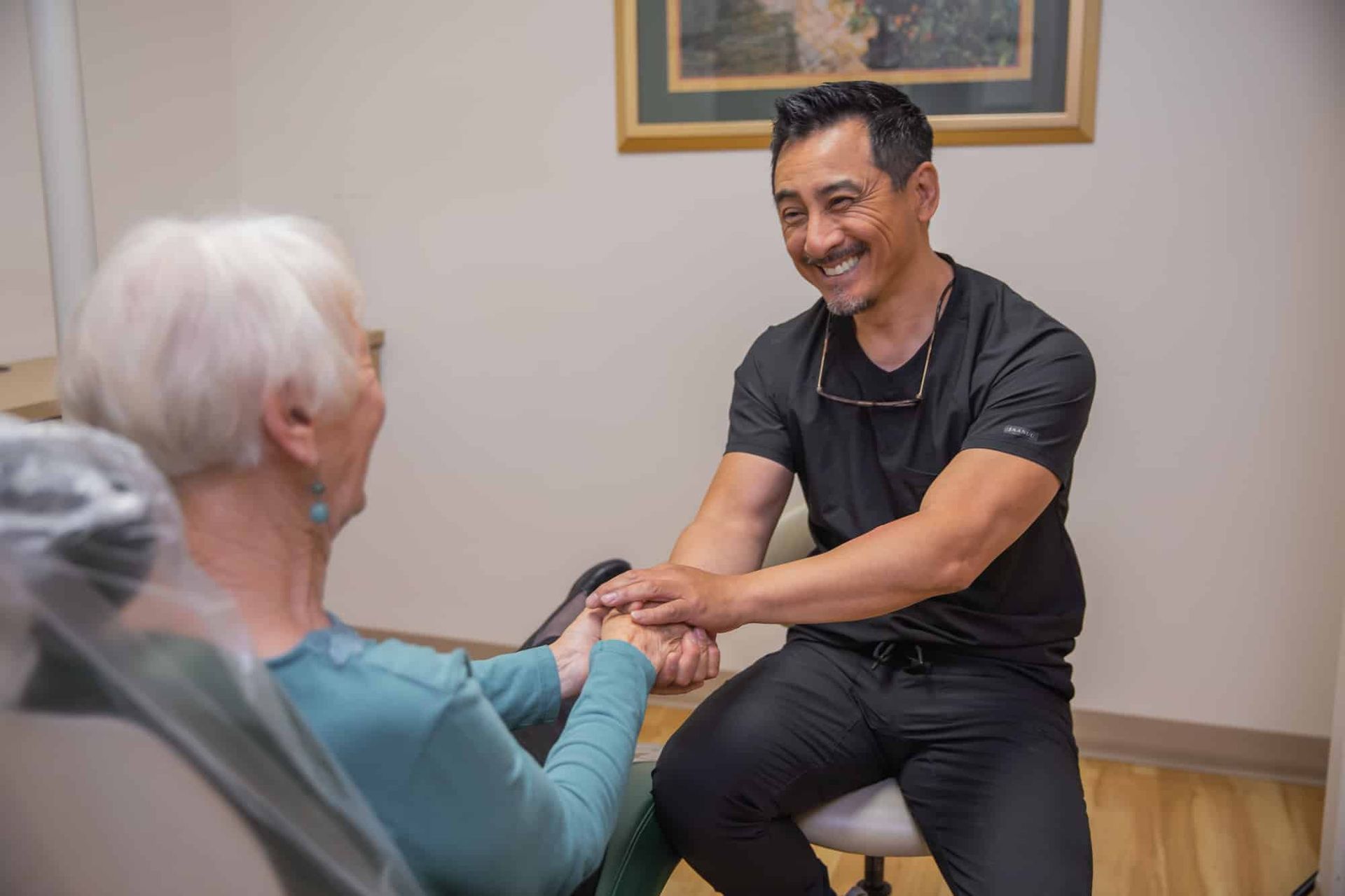 A dentist is shaking hands with an older woman in a dental chair.