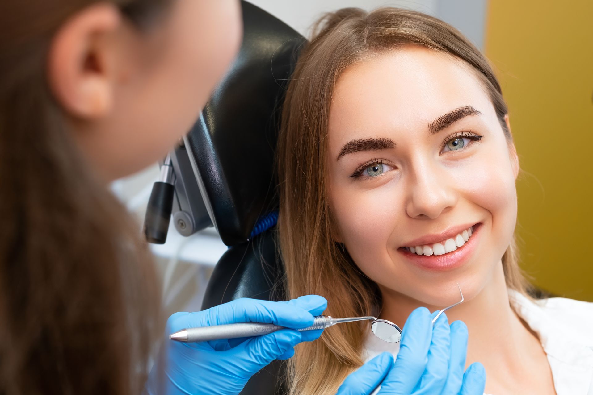 Woman smiling during dental checkup, dental tools visible, blue gloves.