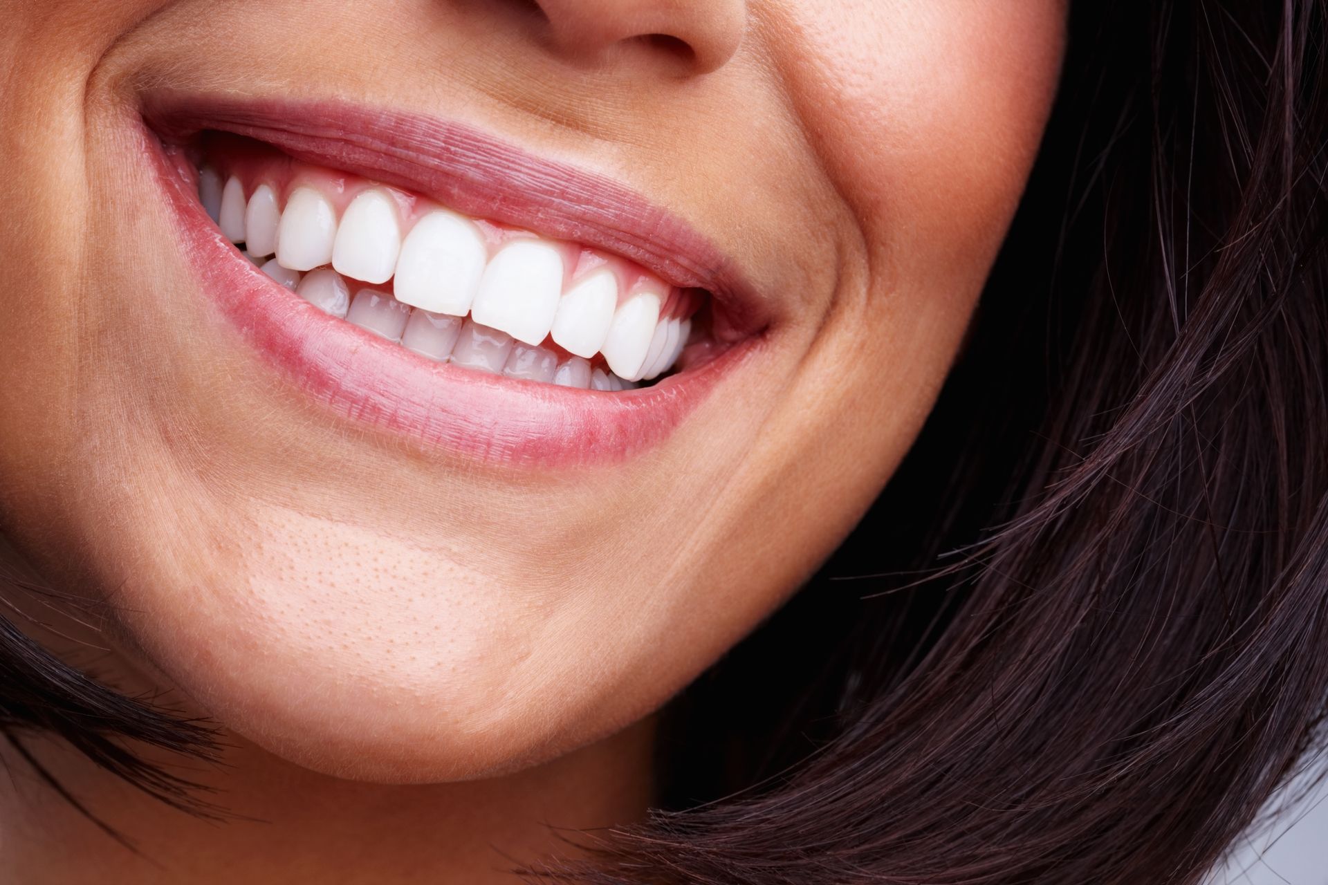 Close-up of a smiling mouth with white teeth and pink lips on a dark background