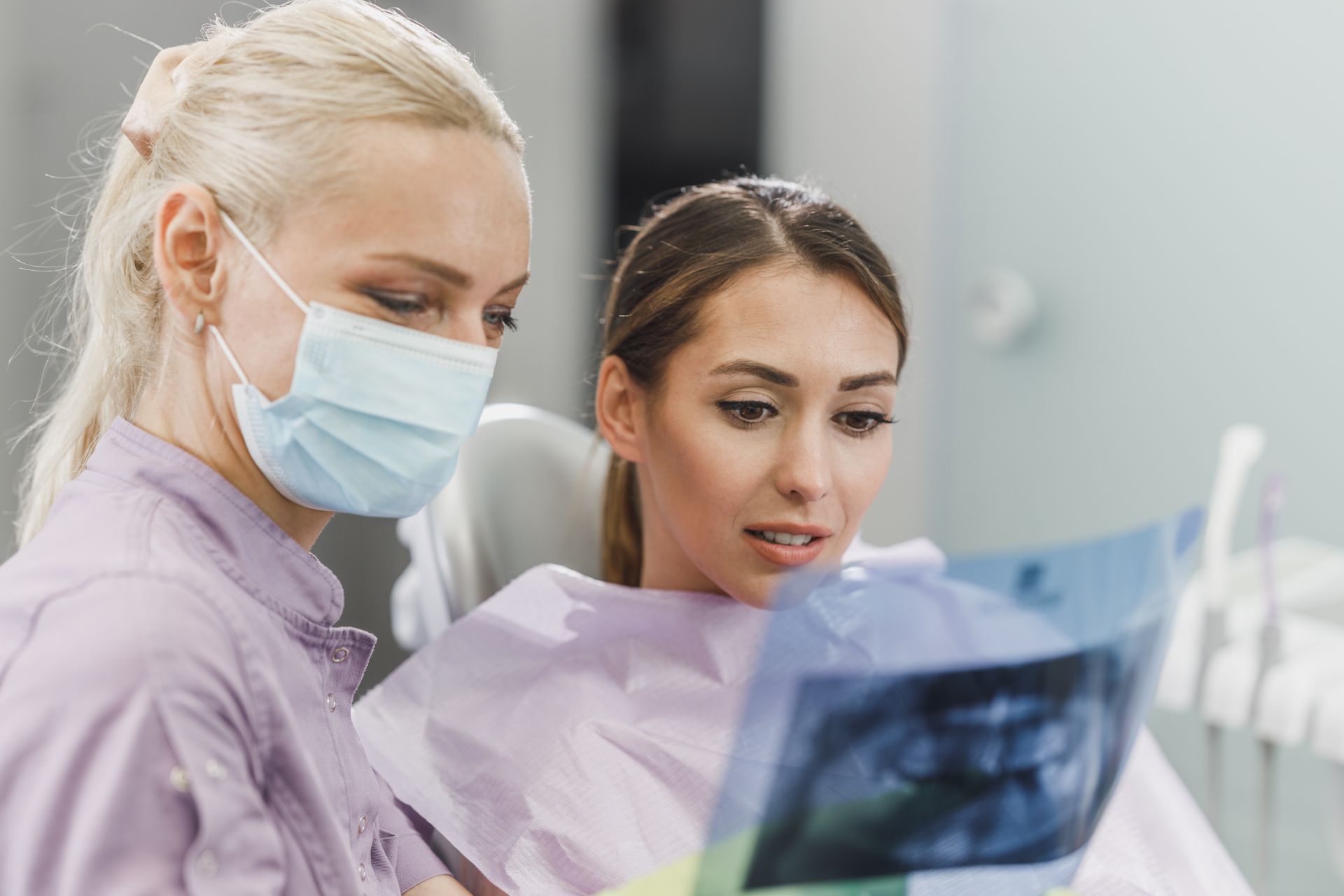 Two dental professionals reviewing an X-ray beside a patient in a clinic