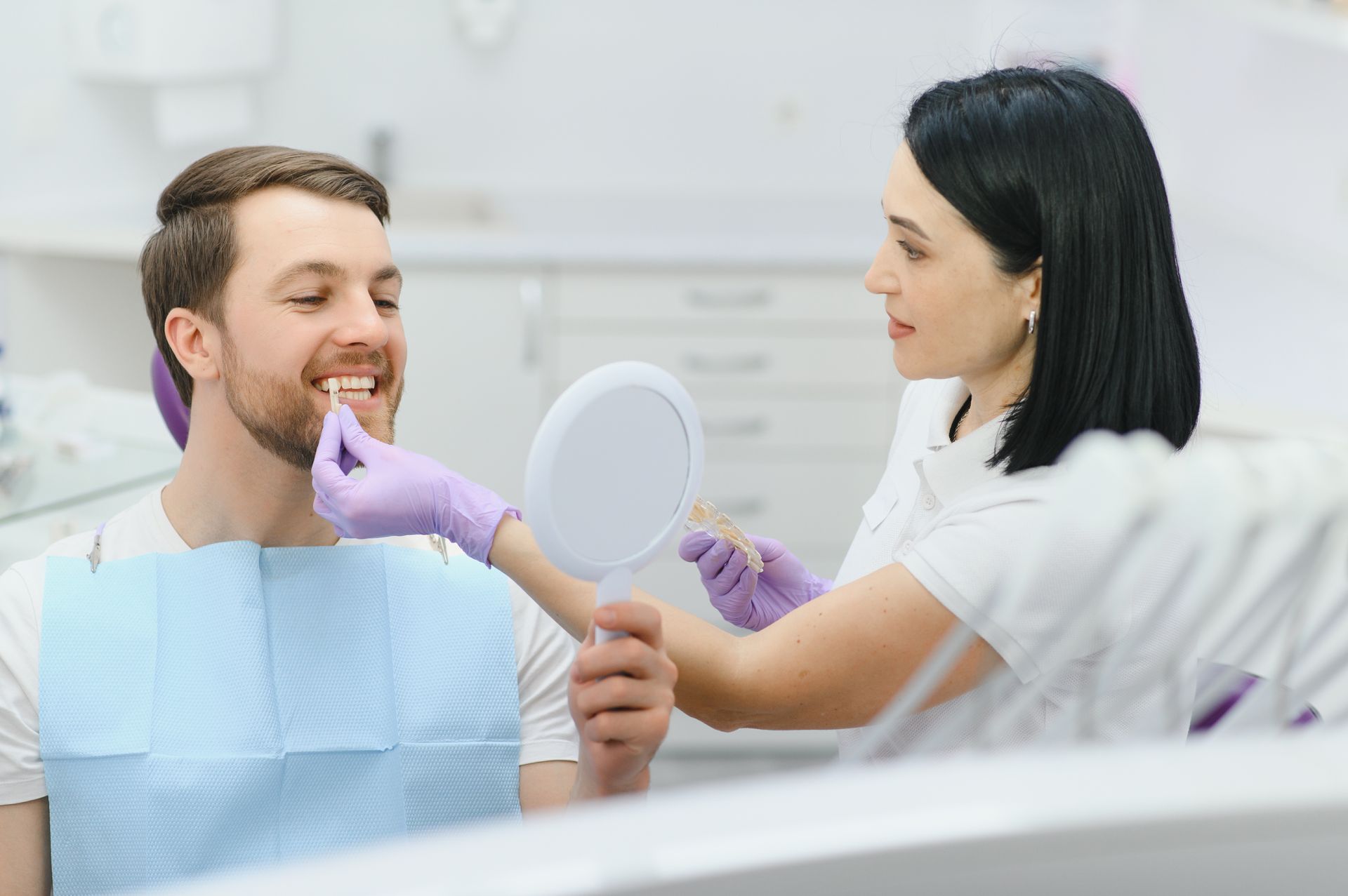 Dentist examining a smiling patient with a mirror in a bright dental clinic