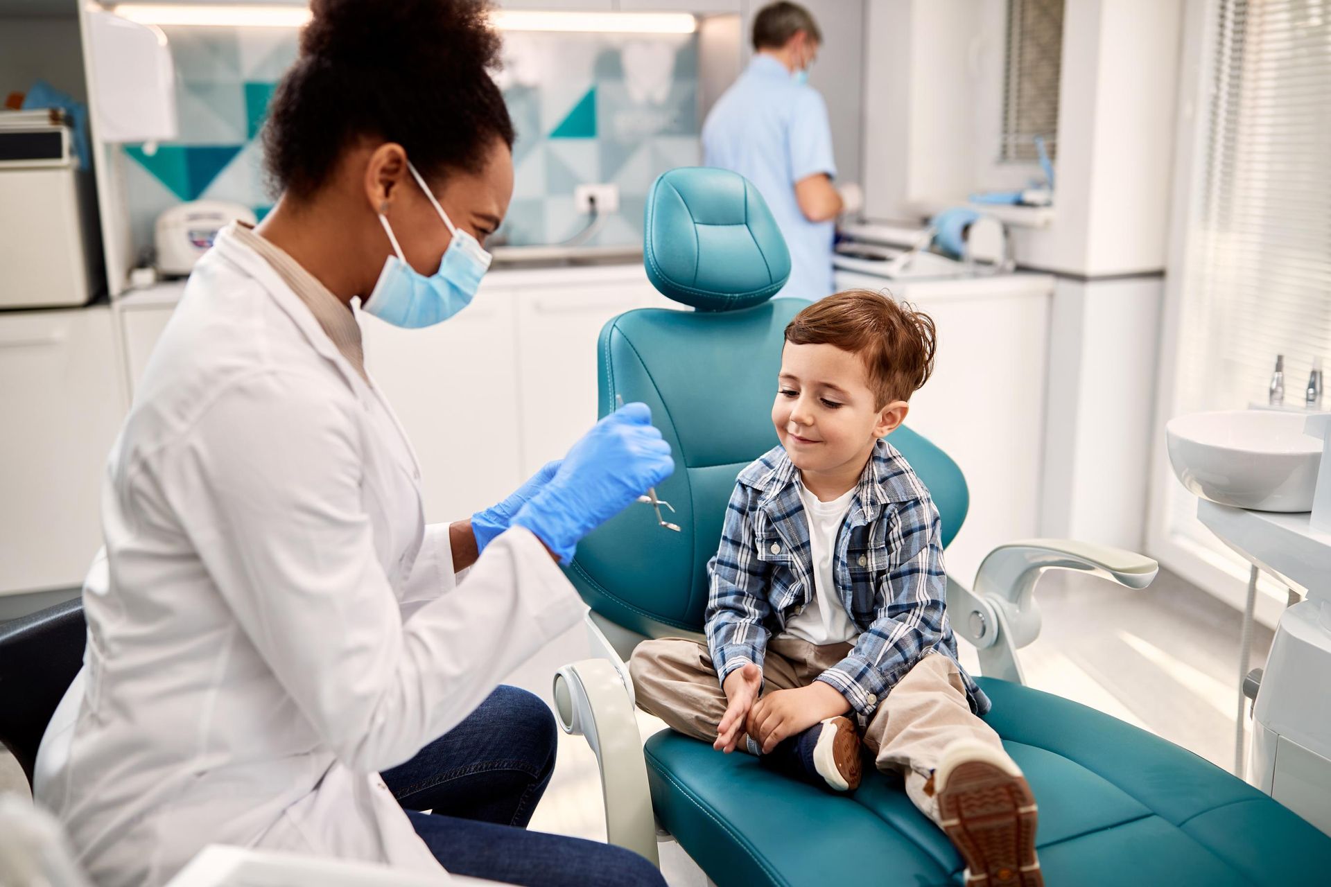 A little boy is sitting in a dental chair while a dentist examines his teeth.