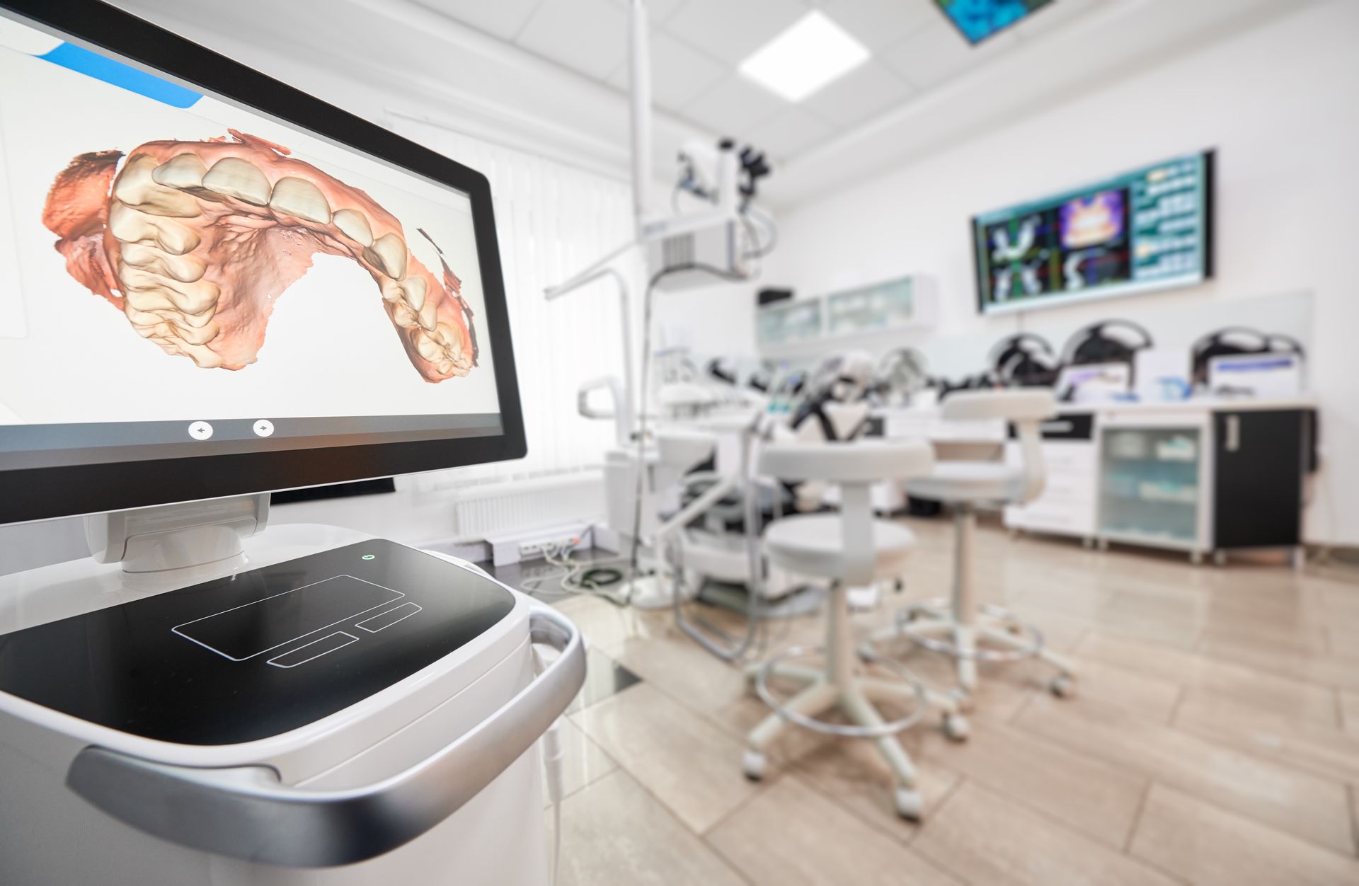 Dental office with a 3D scan on a screen; equipment and chairs in the background.