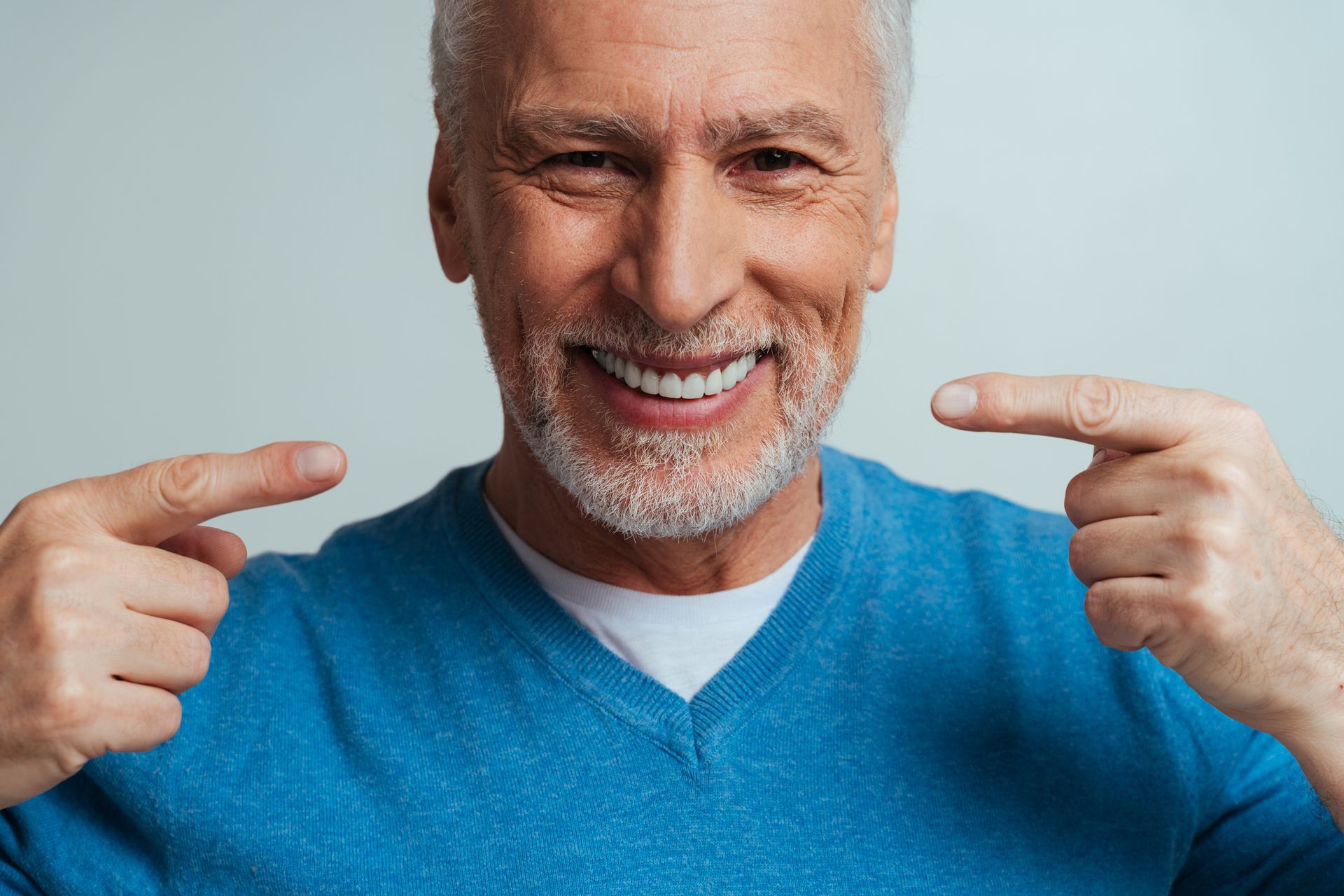 Smiling man in a blue sweater pointing at his teeth with both hands