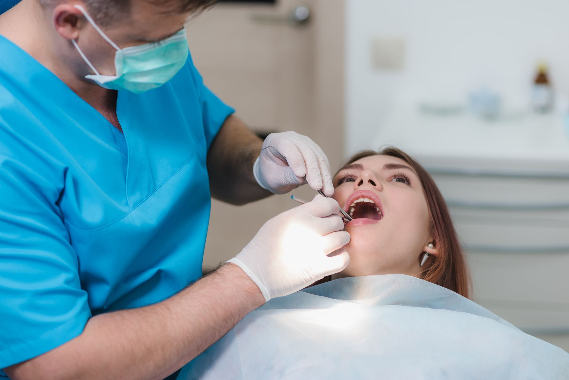 Dentist examining a patient's mouth with tools in a dental office. The patient has open mouth.