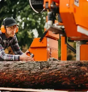 Un homme portant des écouteurs et un chapeau coupe une bûche avec une machine orange.