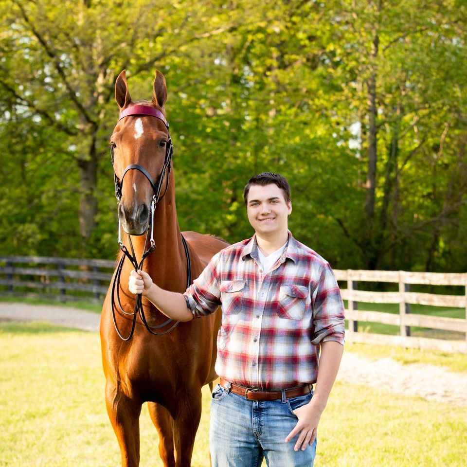 Man in plaid shirt and jeans stands beside a brown horse outdoors.