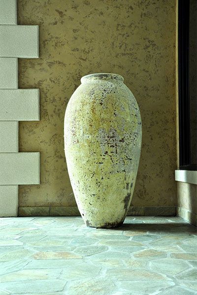 A large vase is sitting on a tiled floor in front of a wall.