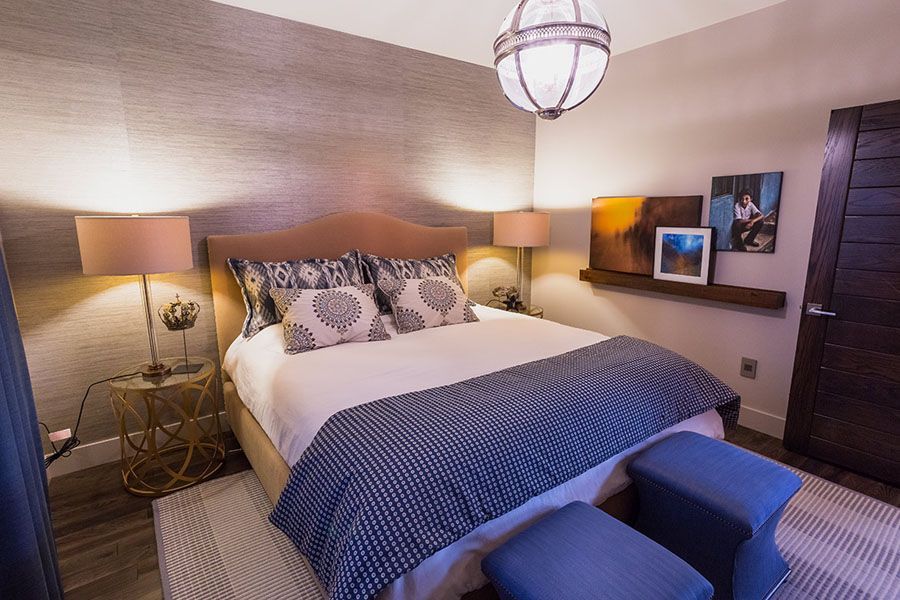 A bedroom with a bed , lamps , ottomans and a chandelier.