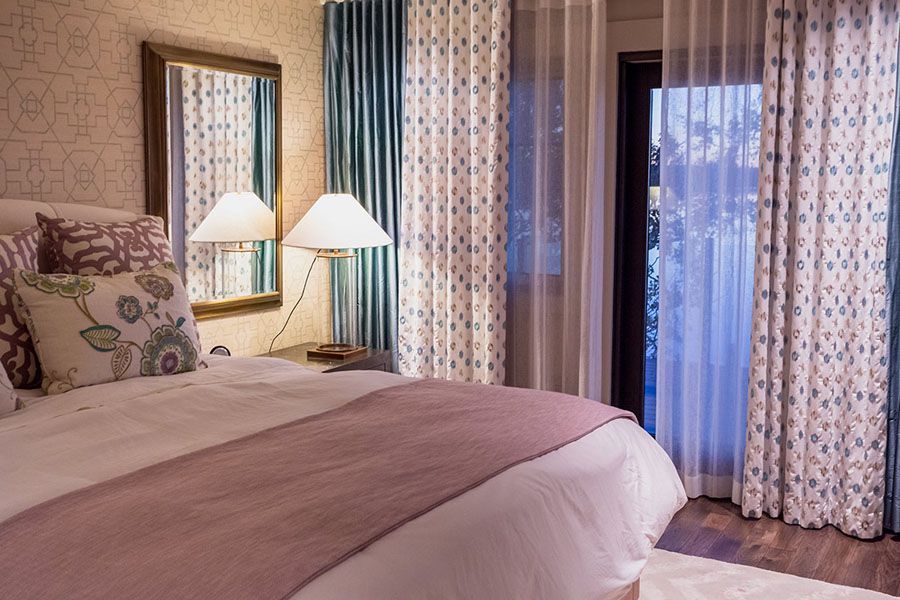 A bedroom with a bed , mirror , lamp and curtains.