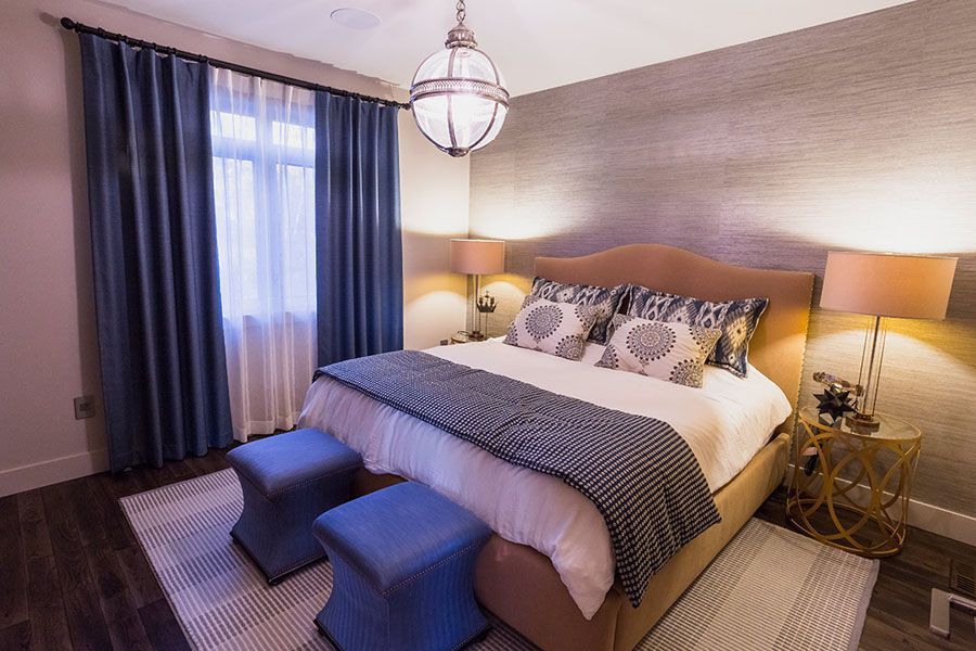 A bedroom with a bed , two ottomans , lamps , curtains and a window.