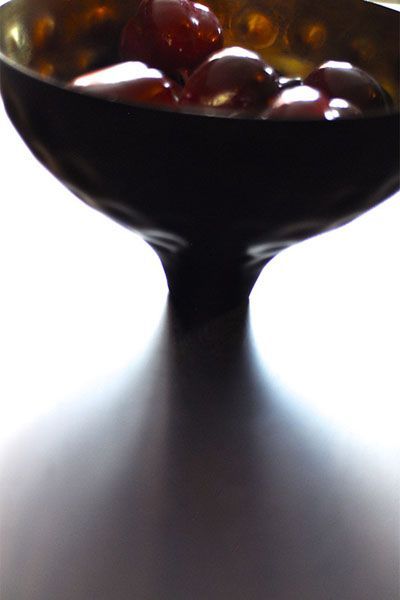 A bowl of cherries sits on a white surface