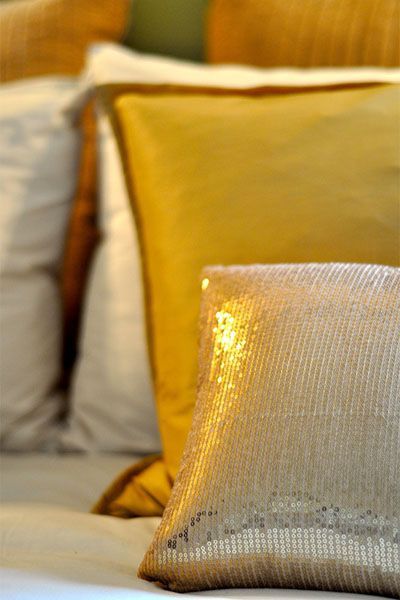 A gold pillow is sitting on a bed next to a yellow pillow.